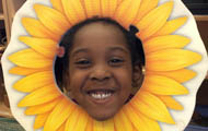 child's smiling face framed by a hand-drawn paper sunflower
