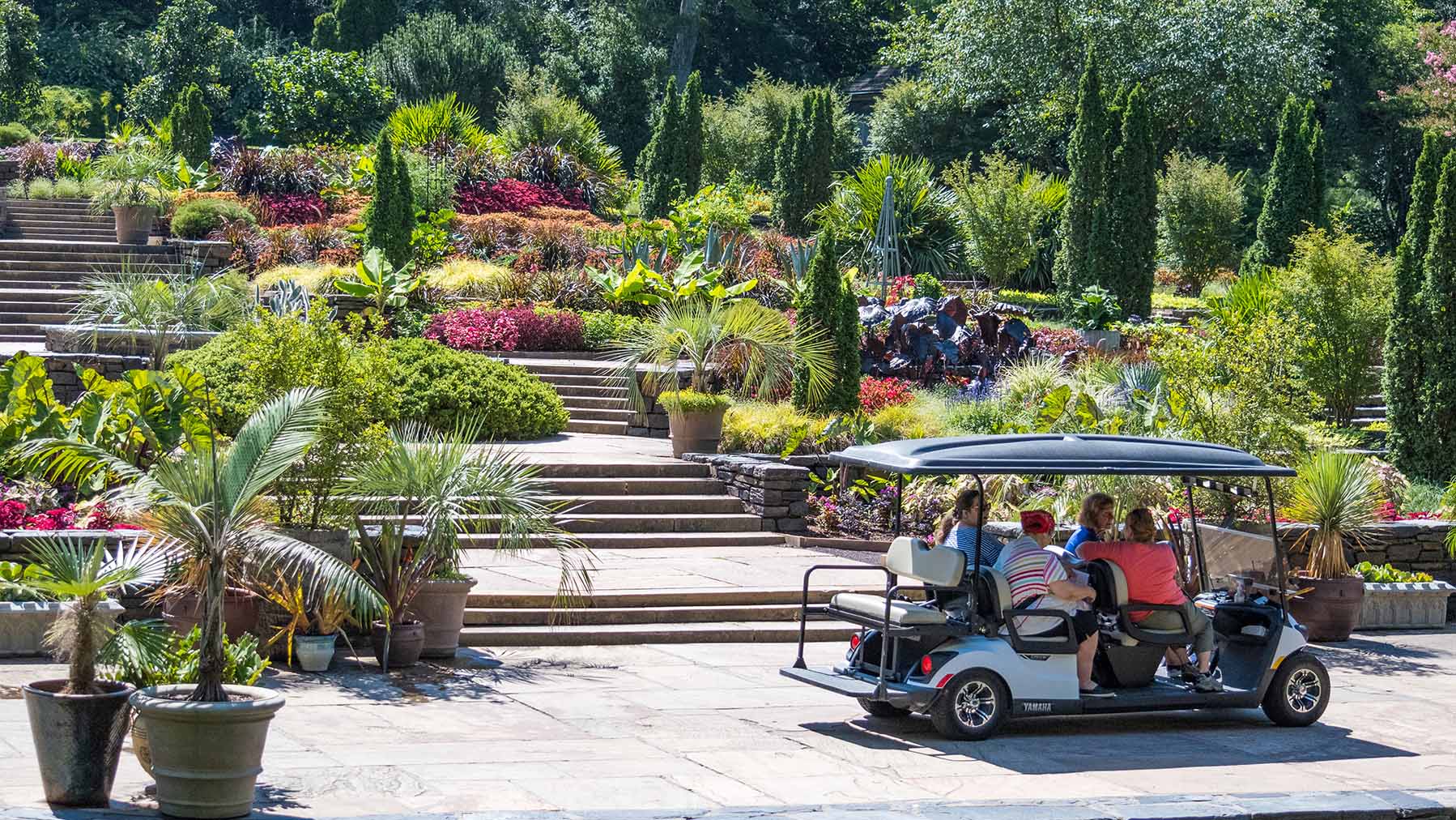 A large terraced garden with a pergola at the top, cherub fountains in the middle, and a golf cart with people in it at the bottom.