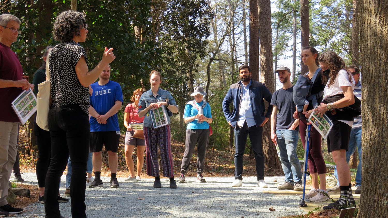 A group of people outdoors listen to Kavanah Anderson, who leads the Midday Meander program.