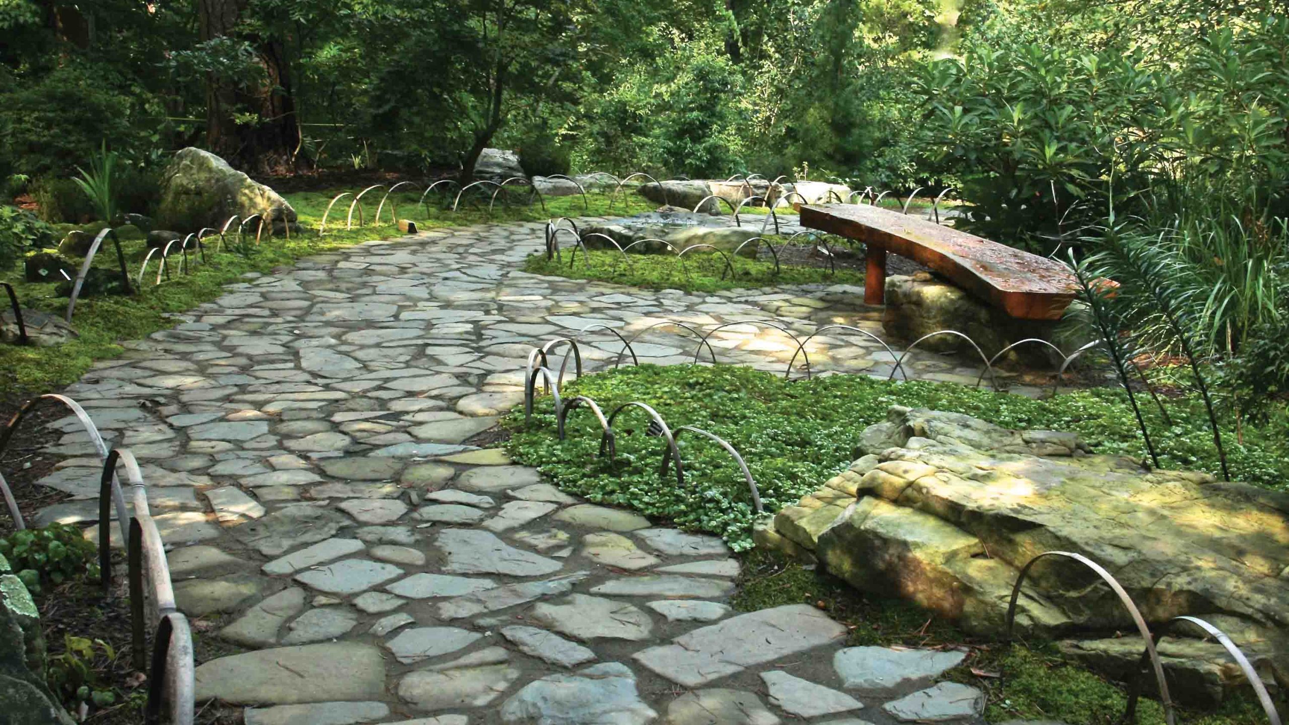 A stone path lined with small bamboo arches curves through a moss garden.