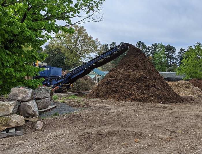 An industrial machine drops mulch into a pile.